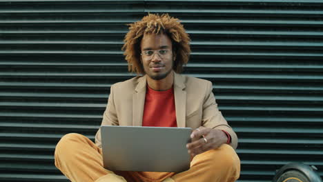 Portrait-of-Young-African-American-Man-Sitting-on-Street-with-Laptop